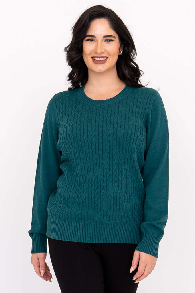 Woman wearing a teal cable knit crew neck sweater with ribbed cuffs, front view