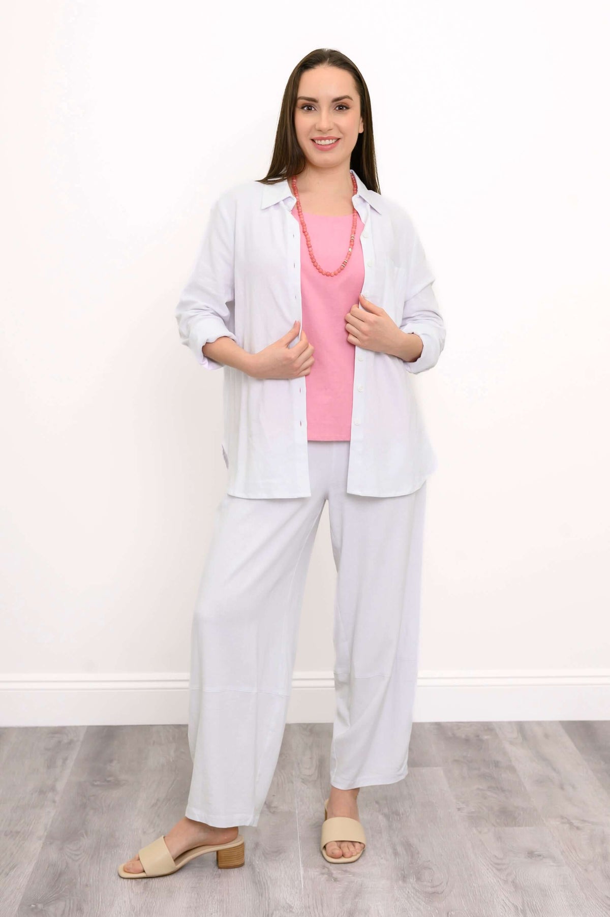Woman wearing wide-leg white pants with a pink top and white button-up shirt