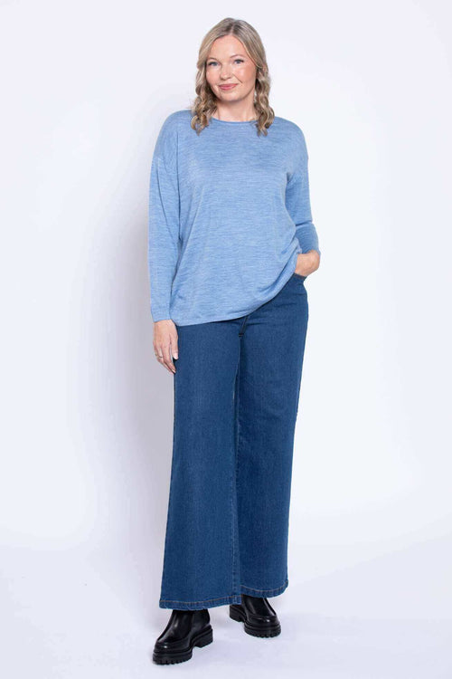 Woman wearing wide leg denim jeans and a light blue top, frontal view
