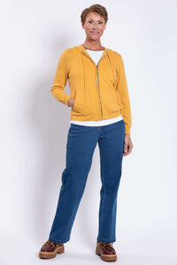 Woman standing in a yellow wool cashmere hoodie, blue jeans, and brown shoes