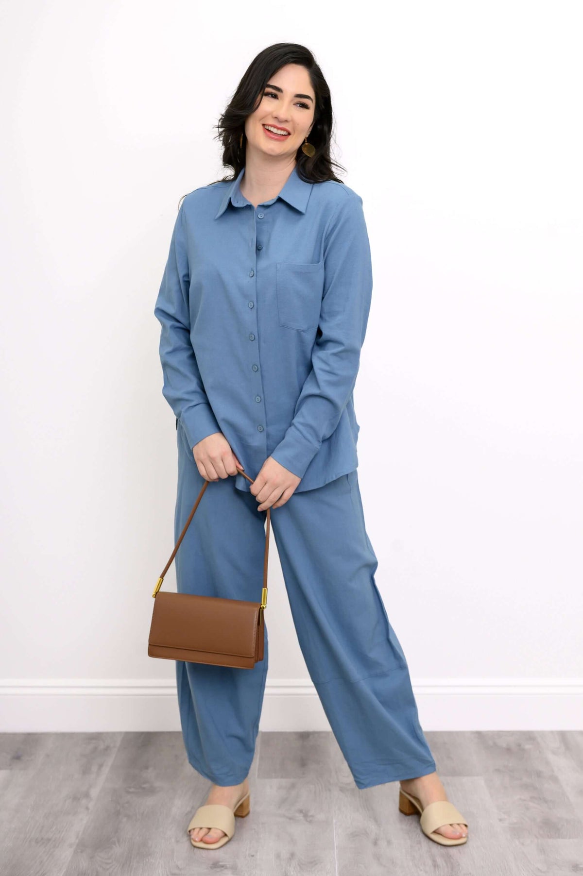 Woman in sky blue shirt and pants holding a brown handbag and smiling