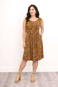 Woman with hand in pocket, showing brown sleeveless floral midi dress with pleats