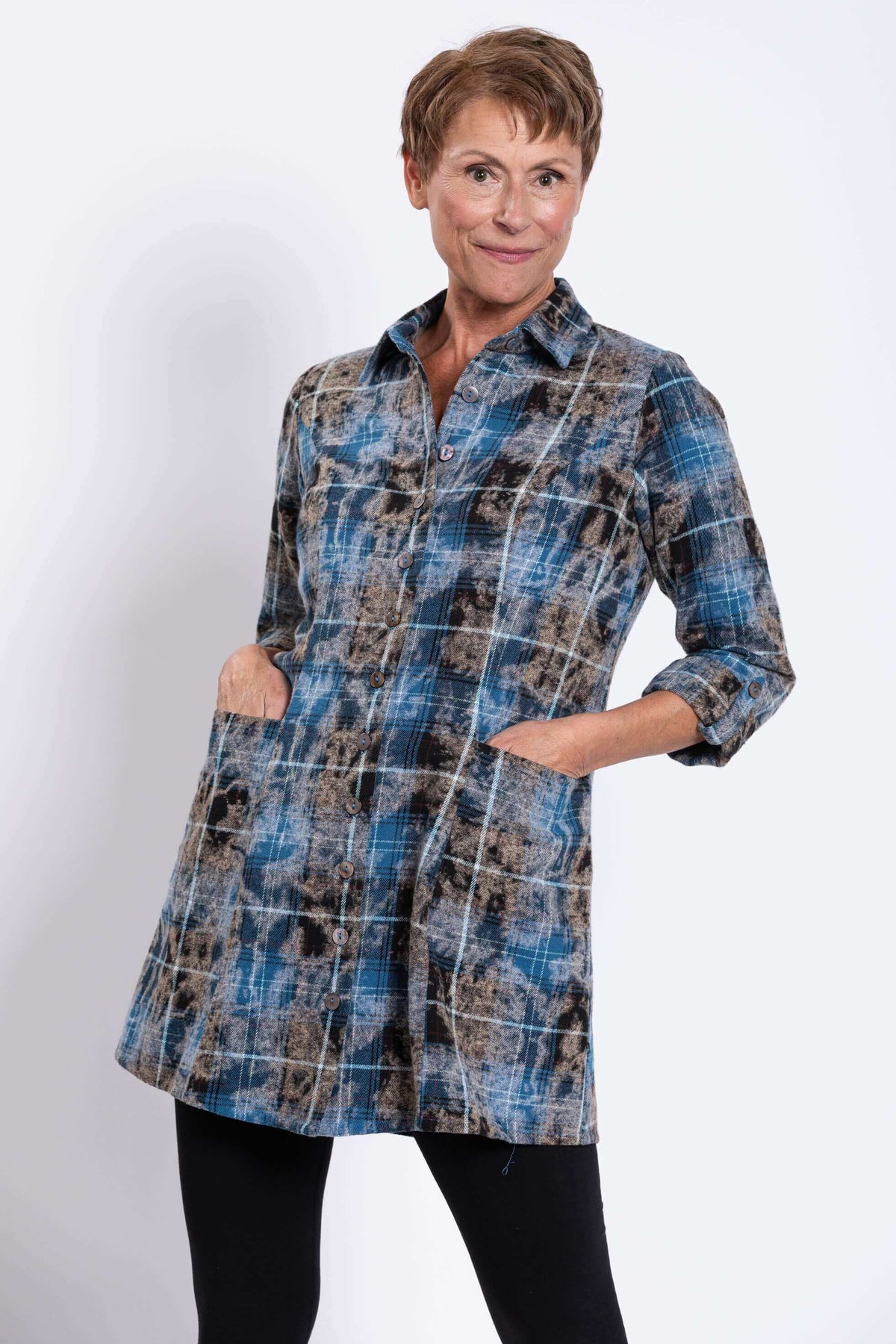 Woman with hands in pockets wearing blue and brown plaid button-up flannel tunic