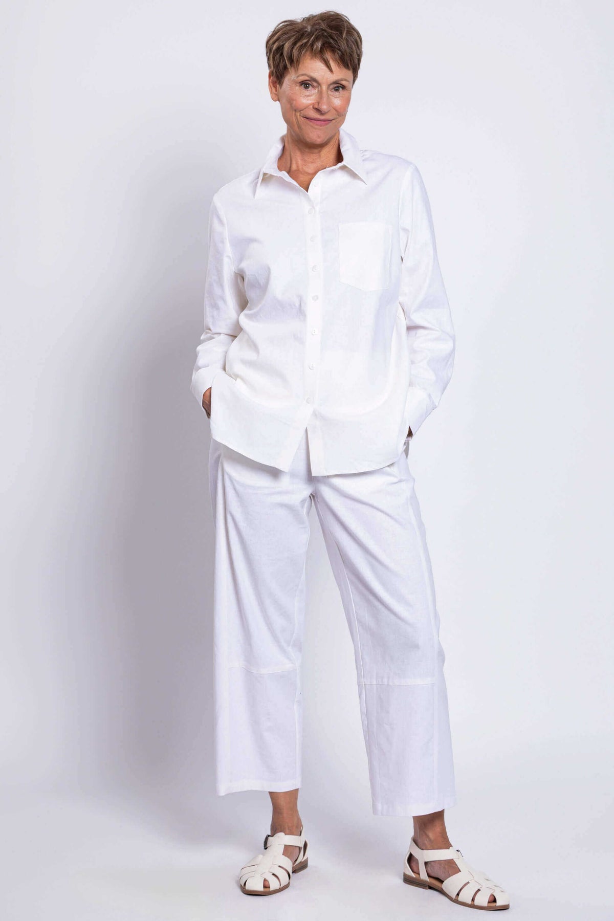 Woman posing hands-in-pockets in a relaxed white shirt and white pants