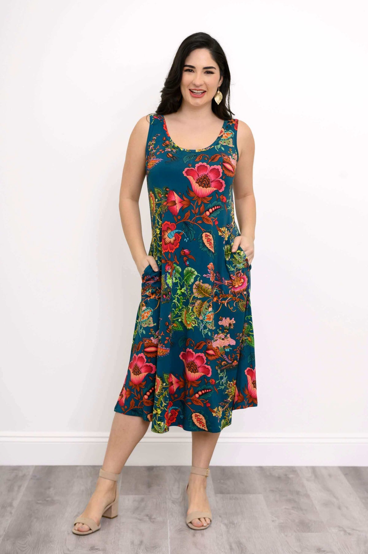 Woman posing with hands in the side pockets of a teal floral tank midi dress