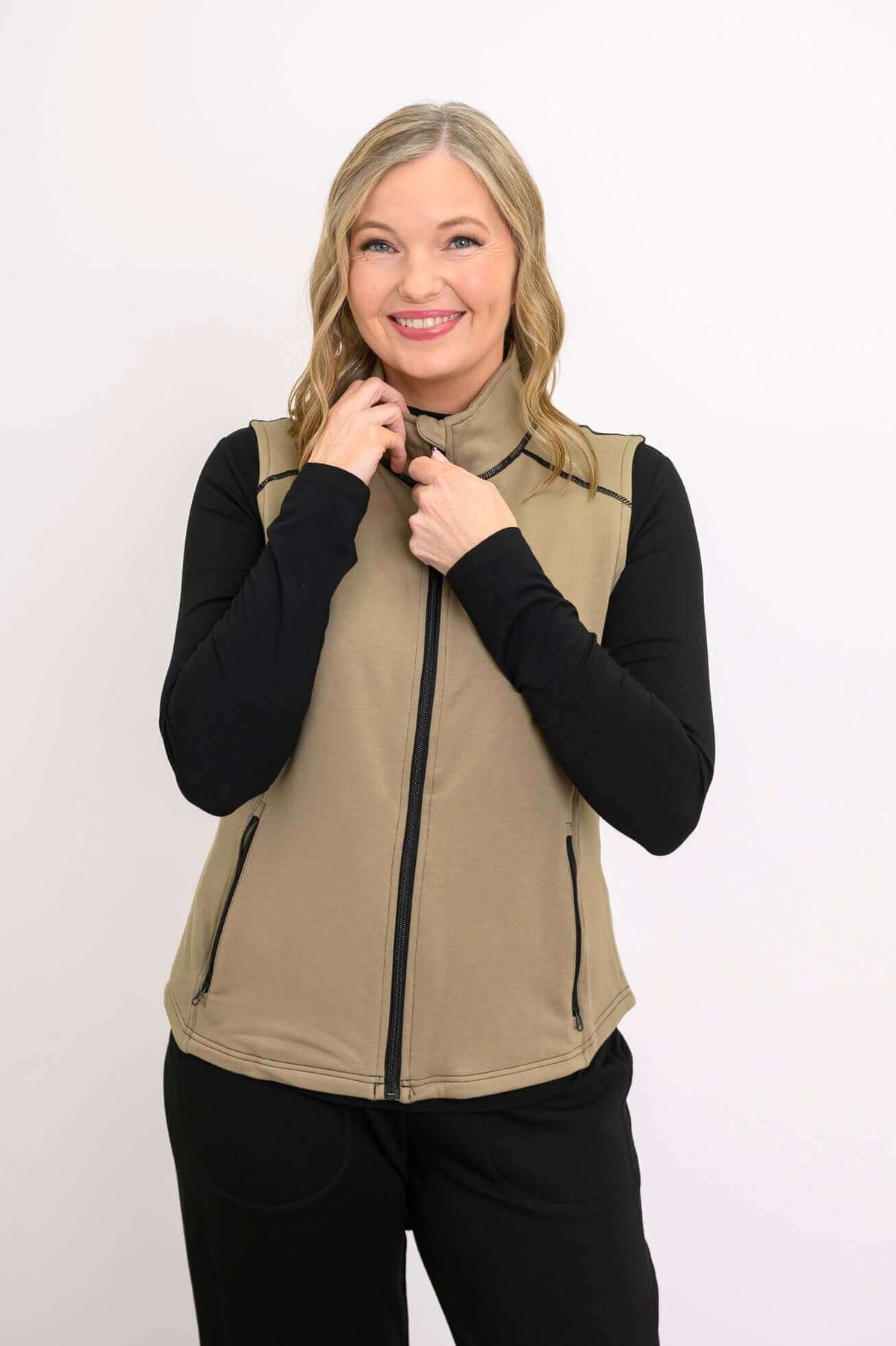 Woman zipping up tan Hartford Utility Vest over black long sleeve top