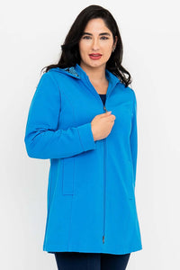 Woman zipping up bright blue thigh-length coat, hood partially visible